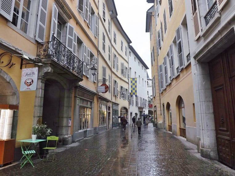 Rue Métropole à Chambéry sous la pluie, pavés luisants et passants au parapluie entre les façades