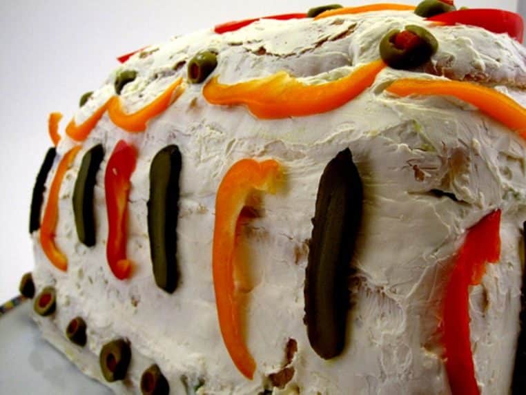 Gros plan sur un pain sandwich garni de fromage à tartiner et de légumes colorés, posé sur une assiette, prêt à être servi au goûter.