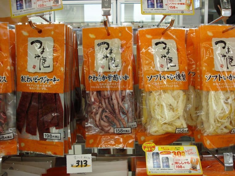 Snacks séchés emballés sous vide dans des sachets orange suspendus en rayon, avec étiquettes japonaises bien visibles.