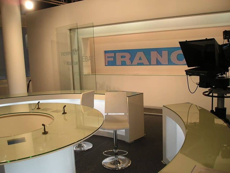 Plateau de studio TV avec caméras et table ronde, décor moderne typique d’une émission d’info.