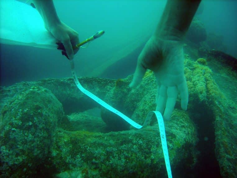 Mesure au ruban d’un élément d’épave sous l’eau, gros plan sur le geste d’un archéologue-plongeur