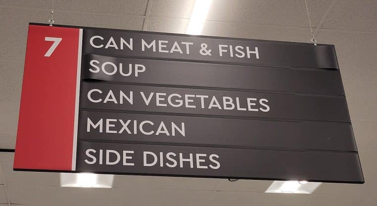 Panneau suspendu indiquant un rayon de supermarché, typographie blanche sur fond noir et repère rouge