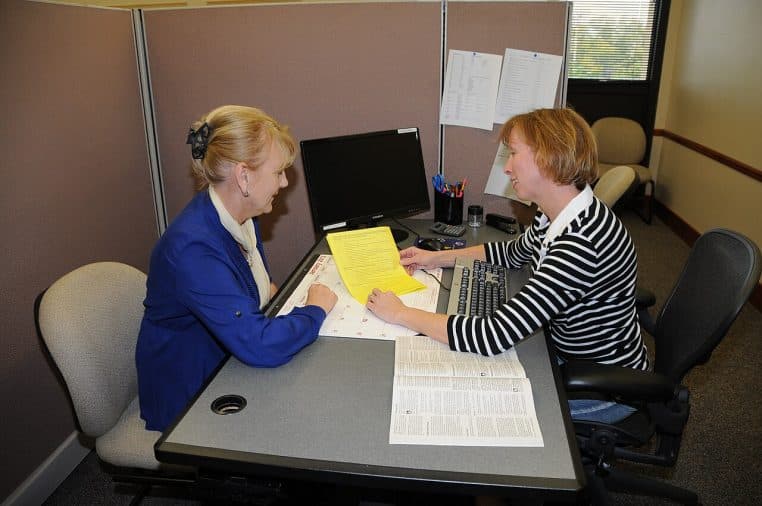 Deux personnes examinant des formulaires fiscaux sur un bureau, scène réaliste de vérification de documents administratifs.