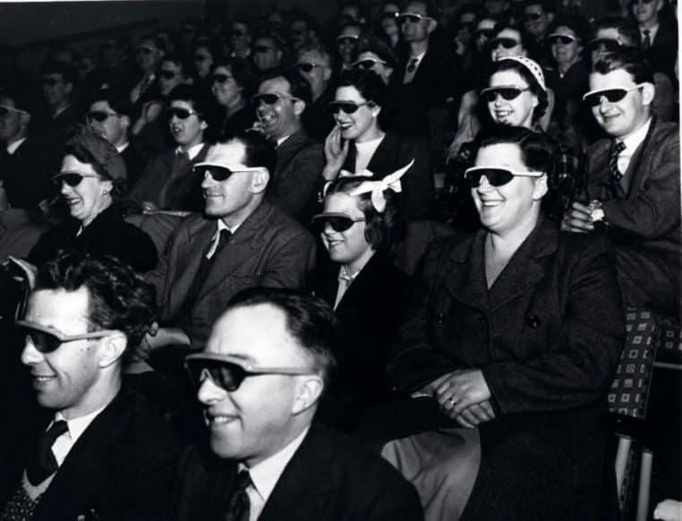 « Public équipé de lunettes 3D pendant une projection, ambiance salle obscure, image d’archive en noir et blanc ».