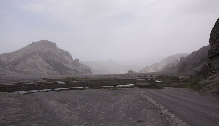 Paysage naturel recouvert de cendres volcaniques, sol gris, reliefs sombres, sensation de “feu et cendres” après éruption