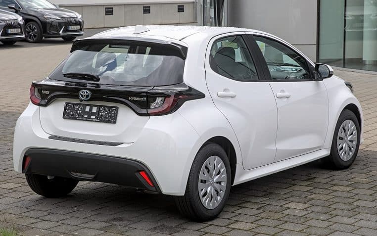 Toyota Yaris hybride blanche vue arrière trois quarts, hayon noir, format citadin et lignes tendues pour la ville.
