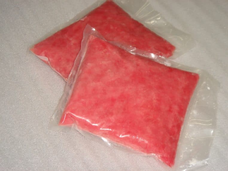 Deux sachets rectangulaires de thon cru emballé sous vide, couleur rose, posés sur une surface blanche légèrement granuleuse.