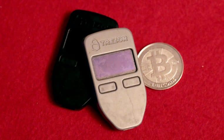 Deux portefeuilles matériels Trezor et une pièce physique Bitcoin posés sur un tissu rouge, gros plan.