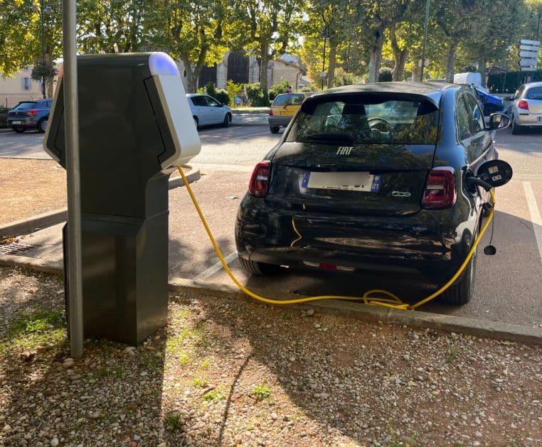 Voiture électrique branchée à une borne de recharge sur un parking français, photographiée en format horizontal.