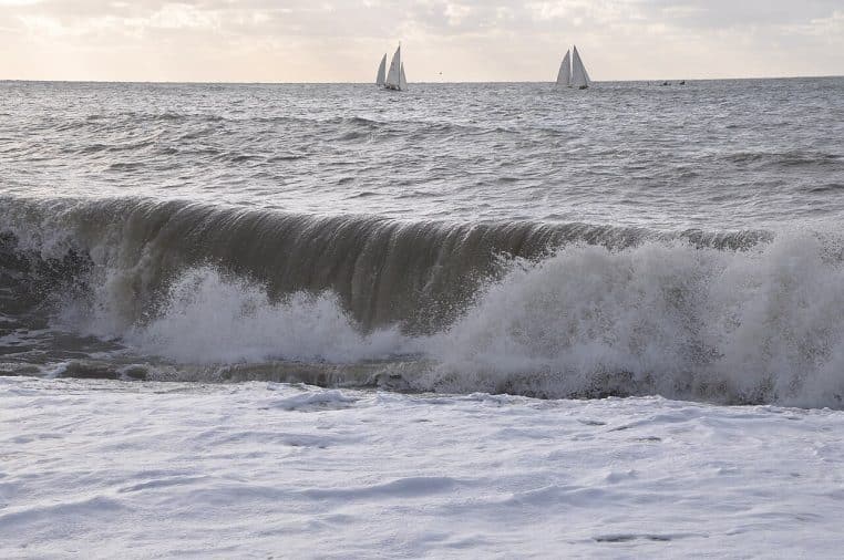 Vague brisant sur la plage du Havre, écume au premier plan, deux voiliers au loin et mer agitée
