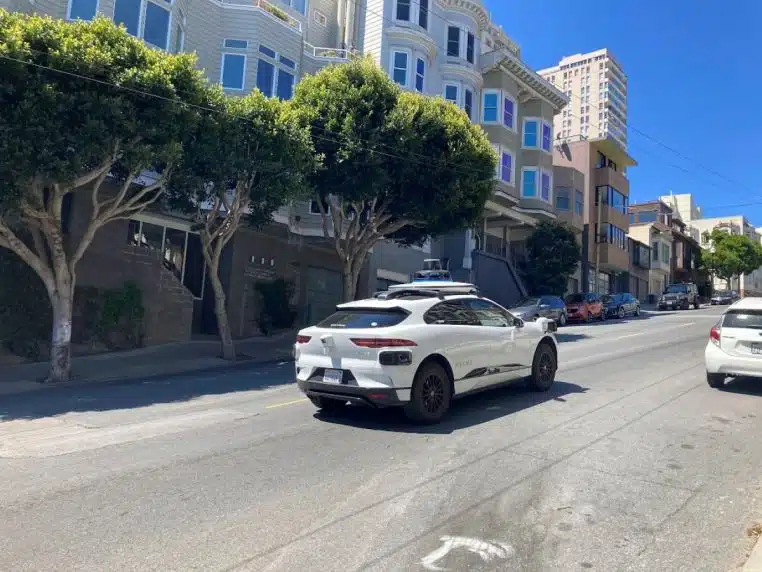 SUV Waymo autonome circulant sur une grande avenue de San Francisco, entouré d’immeubles et de végétation en pleine journée ensoleillée.