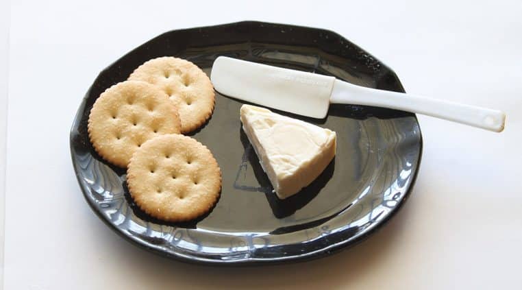 Portion triangulaire de fromage La Vache qui rit posée sur une assiette, emballage aluminium retiré, prête à être dégustée.