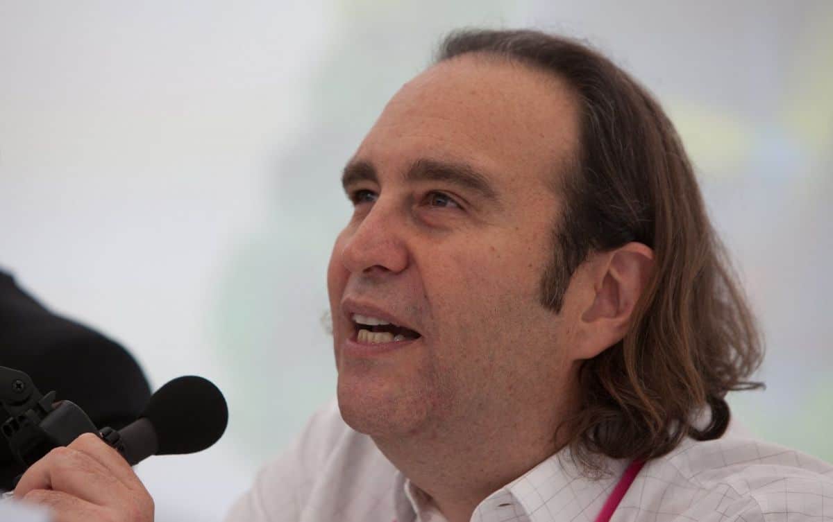 Portrait de Xavier Niel en costume sombre lors d’un événement public, debout de profil sur scène, éclairé par des projecteurs.
