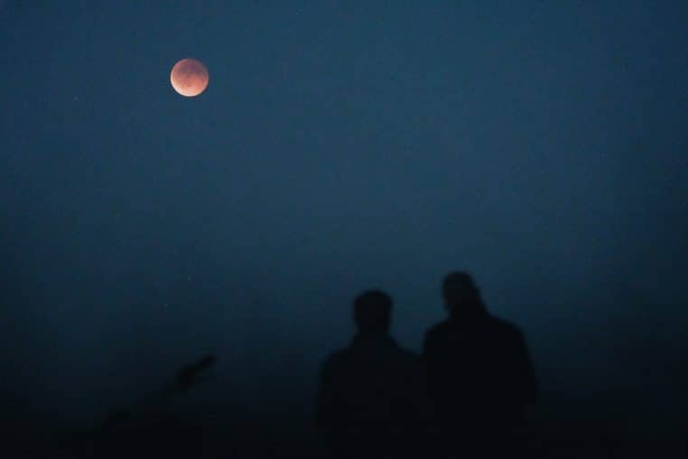 Two people watch a lunar eclipse in the night sky