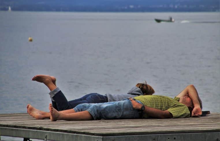 Un couple allongé au bord de l’eau, déconnecté des écrans, pour rappeler l’importance de vraies pauses ensemble.