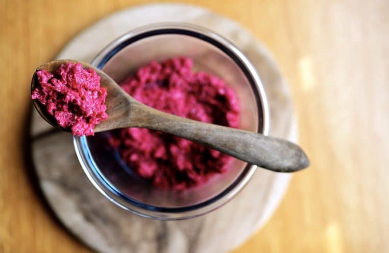 Vue rapprochée d’un bol de salade de betterave violette crémeuse, avec une cuillère en bois posée au-dessus du bol.