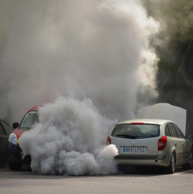 Voiture à l’arrêt sur la route avec un important nuage de fumée sombre sortant de l’échappement, symbole de pollution élevée