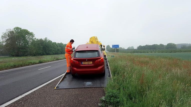 Automobiliste en panne sur le bas-côté près d’un triangle de signalisation rouge placé derrière la voiture arrêtée