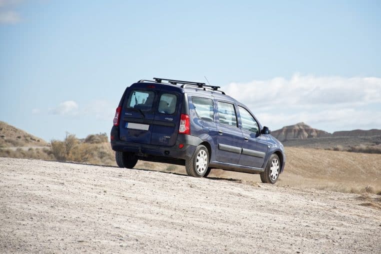 Minivan clair stationné sur une piste en plein désert, isolé dans un paysage minéral baigné de soleil.