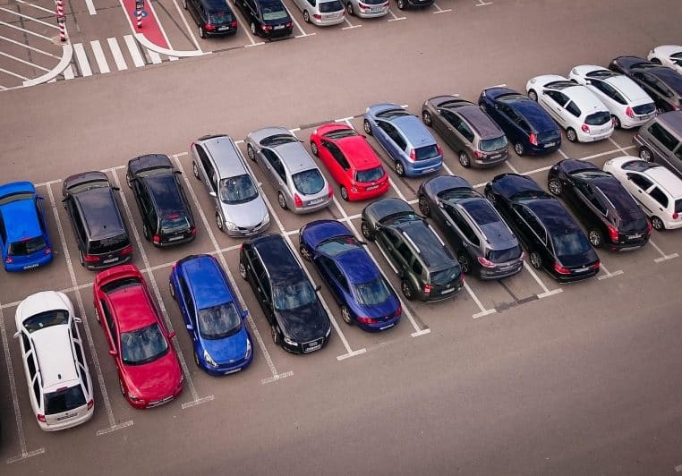 Rangée de voitures garées sur un grand parking extérieur, vue aérienne montrant la diversité des silhouettes.
