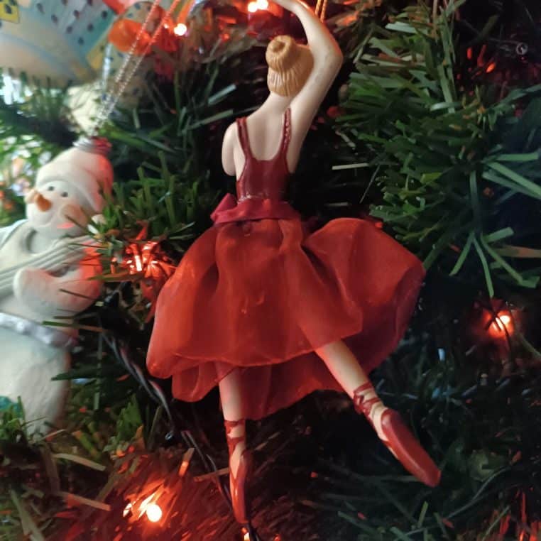 eune femme assise seule près d’un sapin décoré à Noël, regard vers le sol, ambiance douce mais mélancolique dans le salon.