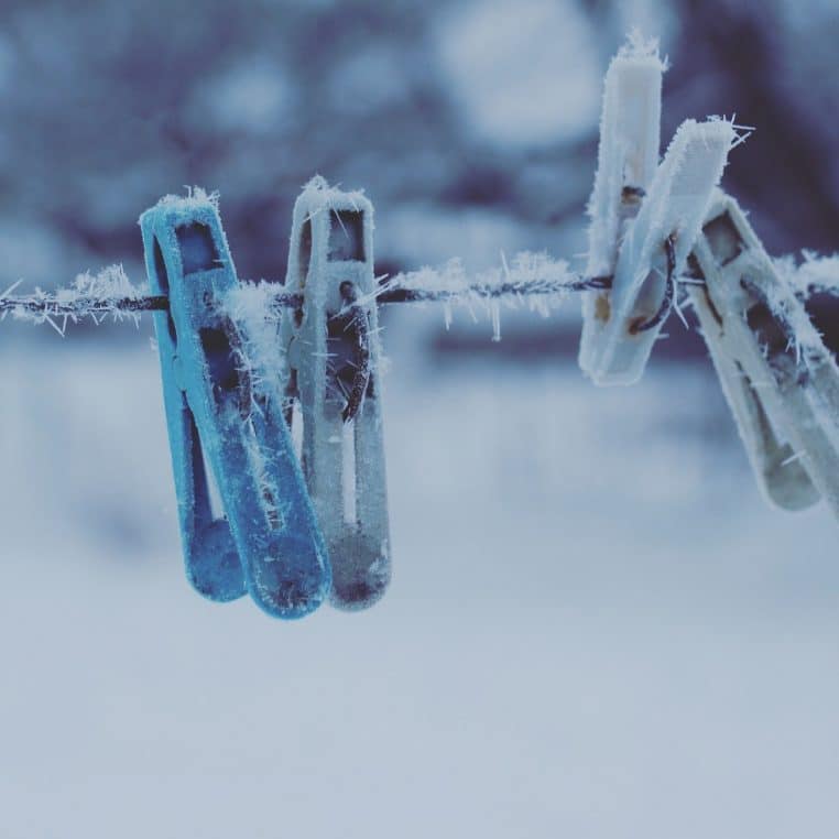 Rangée de pinces à linge colorées prises dans le givre, suspendues sur un fil en plein hiver, évoquant une astuce simple contre le froid.
