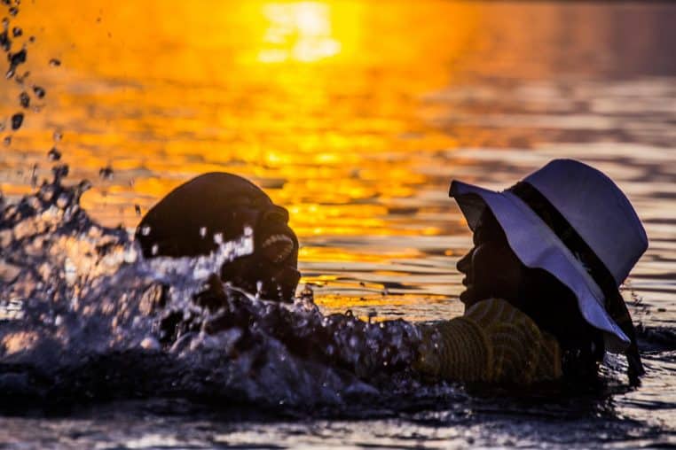 Deux personnes jouent dans l’eau au coucher du soleil, scène de complicité qui fait oublier la pression du quotidien.