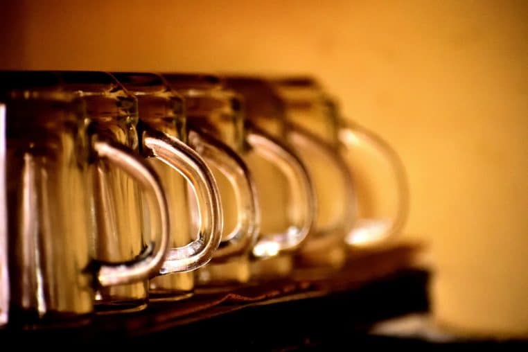 Plusieurs tasses blanches rangées à l’envers sur une étagère en bois, poignées alignées, prêtes à être utilisées dans la cuisine