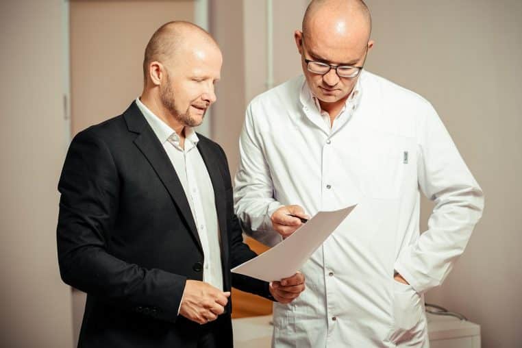 Médecin en blouse blanche expliquant un document à un patient en costume dans un cabinet lumineux lors d’une consultation en face-à-face.