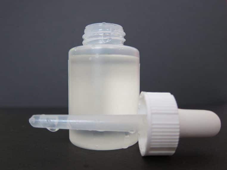 Pot de masque gris et cuillère en bois remplie de produit posés sur un fond en bois clair, évoquant les peelings maison et les soins exfoliants puissants.