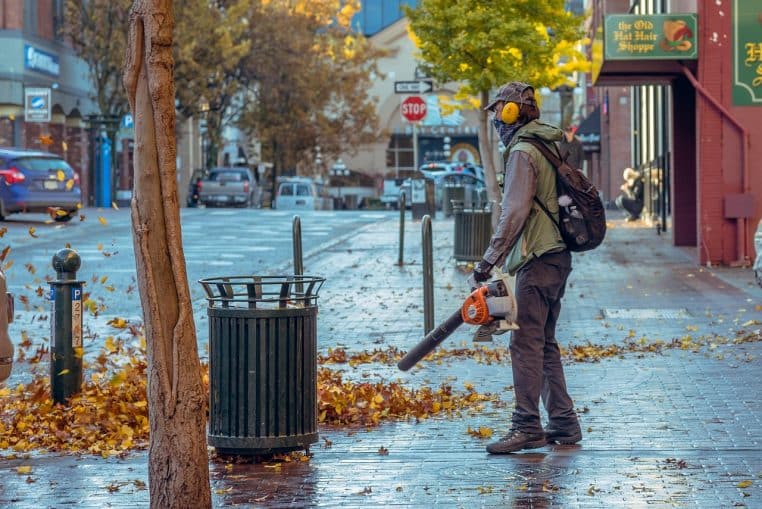 Employé municipal utilisant un souffleur de feuilles sur un trottoir couvert de feuilles jaunes par une matinée d’automne