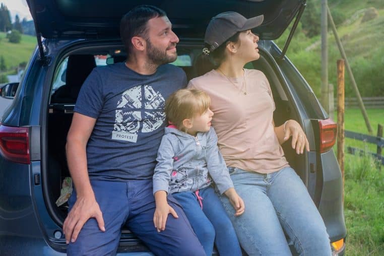 Famille assise dans une voiture moderne à l’arrêt, souriante, prête à partir en voyage sur la route des vacances.