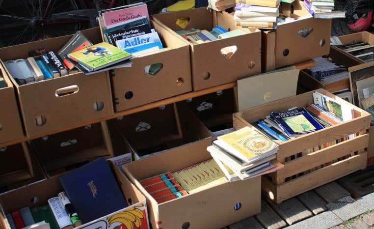 Caisse remplie de livres d'occasion sur un stand de marché aux puces, prête à être vendue pour financer le budget des fêtes.