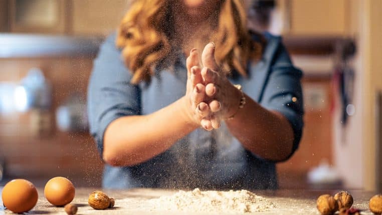 Personne applaudissant ses mains couvertes de farine au-dessus d’un plan de travail de cuisine, image concrète de celui qu’on « roule dans la farine ».