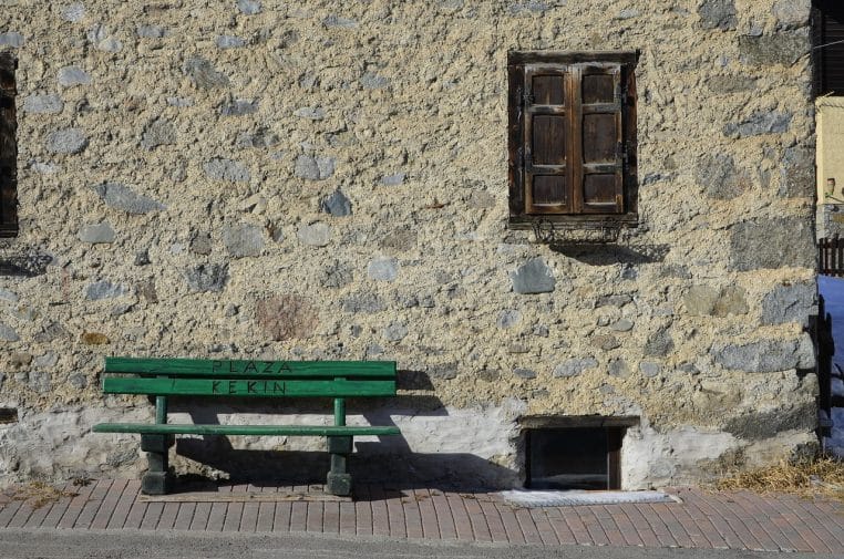 Banc vert en bois devant la façade en pierre d’une maison ancienne, symbolisant la retraite et le temps qui passe dans un environnement calme