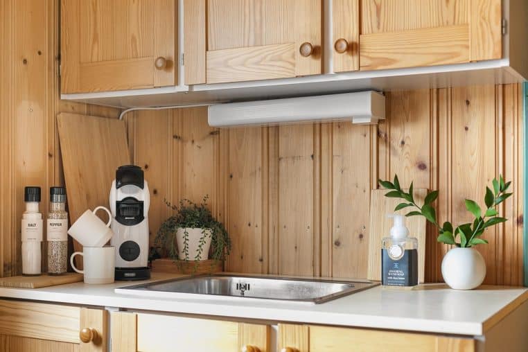 Rangée de tasses et de mugs colorés alignés sur une étagère de cuisine moderne, près d’une machine à café posée sur le plan de travail