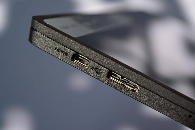 Gros plan en biais sur le bord d’un ordinateur portable noir montrant un port HDMI et un port USB bien visibles sur un fond flou.