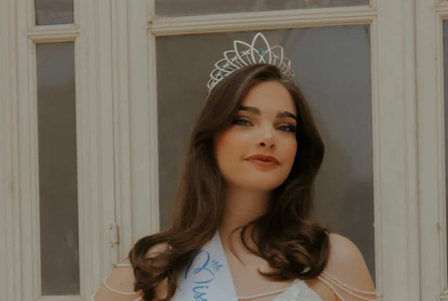 Portrait de Miss Auvergne 2025 portant une couronne et une écharpe blanche, devant une fenêtre claire.