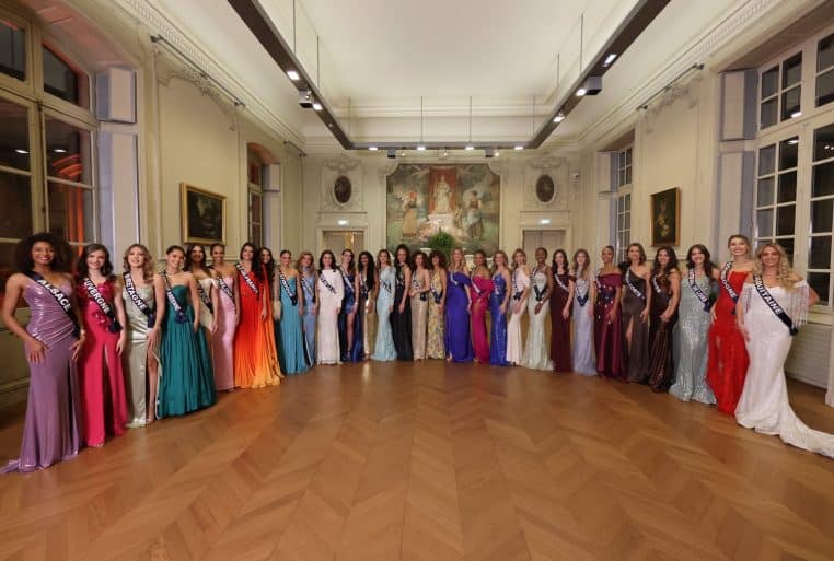 Les trente candidates à Miss France 2026 posent côte à côte en robes de soirée colorées dans un salon au parquet en chevron.
