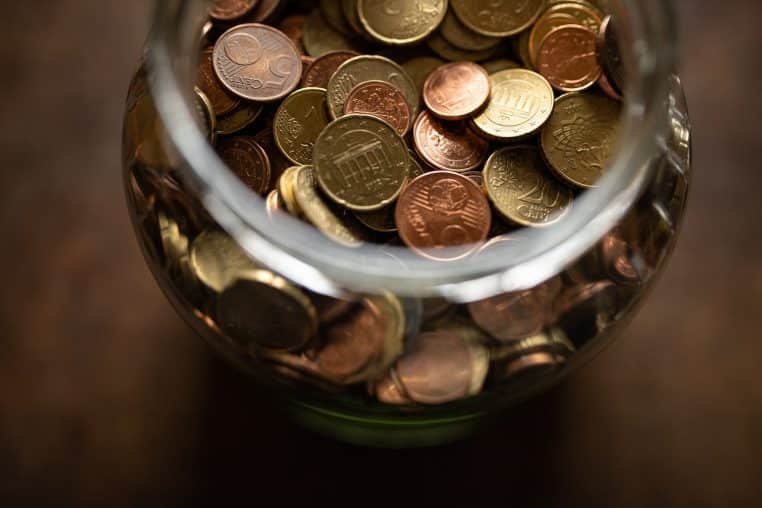 Tirelire rose entourée de pièces de monnaie en euros, représentant la décision de déplacer son argent du compte courant vers l’épargne.