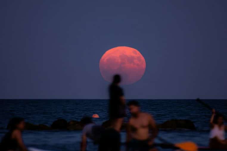 A group of people sitting on a beach under a pink moon