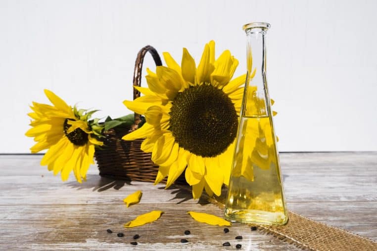 Bouteille d’huile de tournesol posée à côté d’une fleur et de graines, rappelant la présence massive de cette huile dans de nombreux produits transformés
