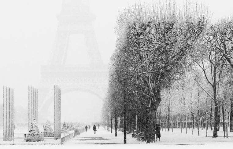 Promeneurs avançant sous une forte chute de neige près de la tour Eiffel, les allées et arbres entièrement recouverts de blanc