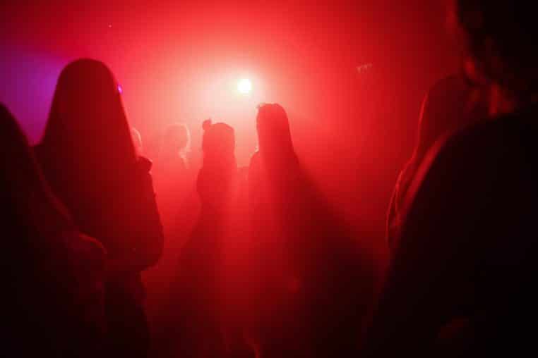 Silhouettes de fêtards dans une lumière rouge intense au milieu de la fumée, évoquant le vacarme d’une soirée qui fait du « barouf
