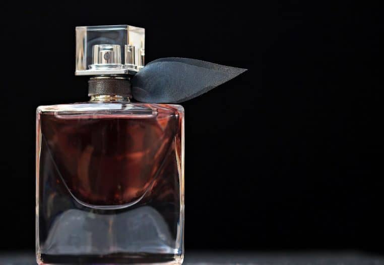 Gros plan sur un flacon de parfum transparent posé sur une surface claire, entouré de pétales roses, avec un éclairage doux façon nature morte.
