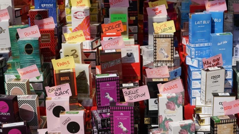 Stand de marché avec plusieurs flacons de parfum alignés, vendeuse en arrière-plan et lumière naturelle mettant en valeur les bouteilles en verre.