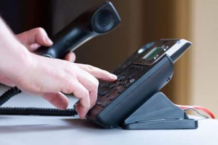 Gros plan sur une main qui compose un numéro sur un téléphone fixe de bureau, combiné décroché, illustrant les appels sortants.