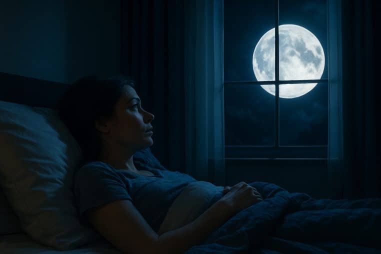 Femme allongée dans un lit, éveillée dans une chambre sombre, une pleine Lune très brillante visible à la fenêtre.