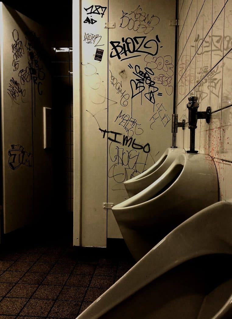 Urinoirs alignés dans des toilettes d’école couvertes de graffitis, ambiance sombre rappelant les sanitaires publics très fréquentés.