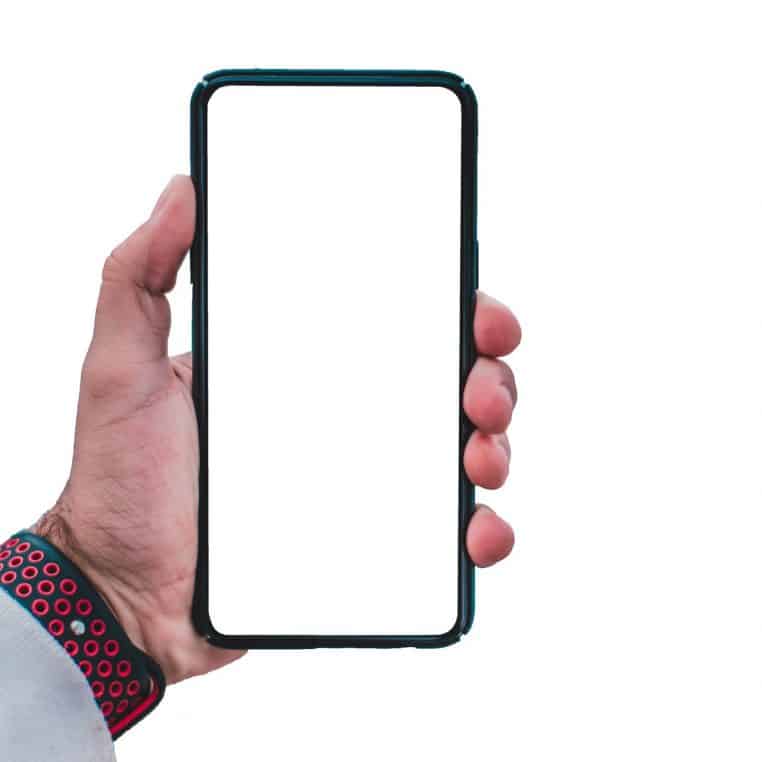 Main d’un adulte tenant un smartphone au grand écran blanc, prêt à afficher un appel inconnu ou un numéro de démarchage.